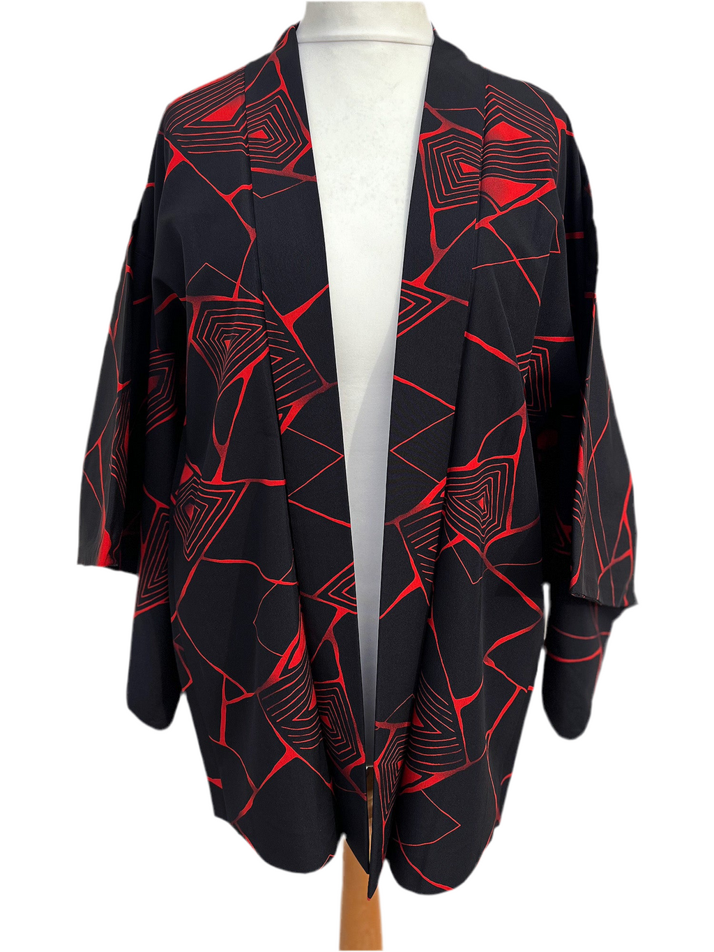 Black kimono-style haori jacket featuring an abstract red geometric pattern, upcycled from vintage Japanese fabric, lightweight and open-front design, displayed on a hanger