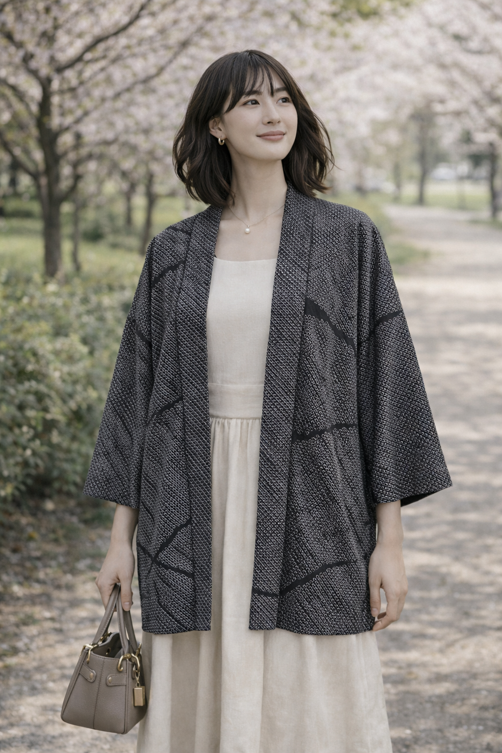 A woman wearing a vintage Japanese haori jacket over a casual date-ready outfit, standing in a spring park with her arms relaxed at her sides; the black shibori-patterned haori falls to mid-thigh, with butterfly motifs hidden at the sleeve hems and not visible from this angle.